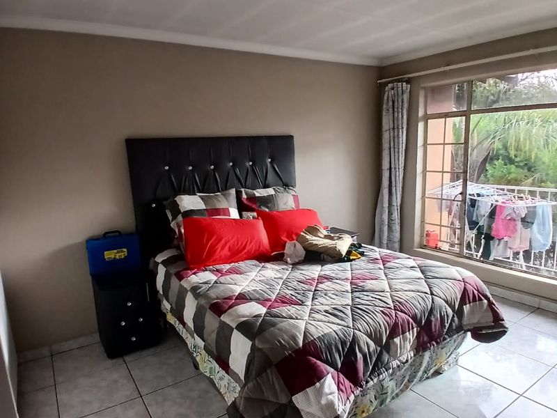 A bedroom featuring tiled flooring, a central ceiling light, and a large window providing natural light and a view of the exterior.