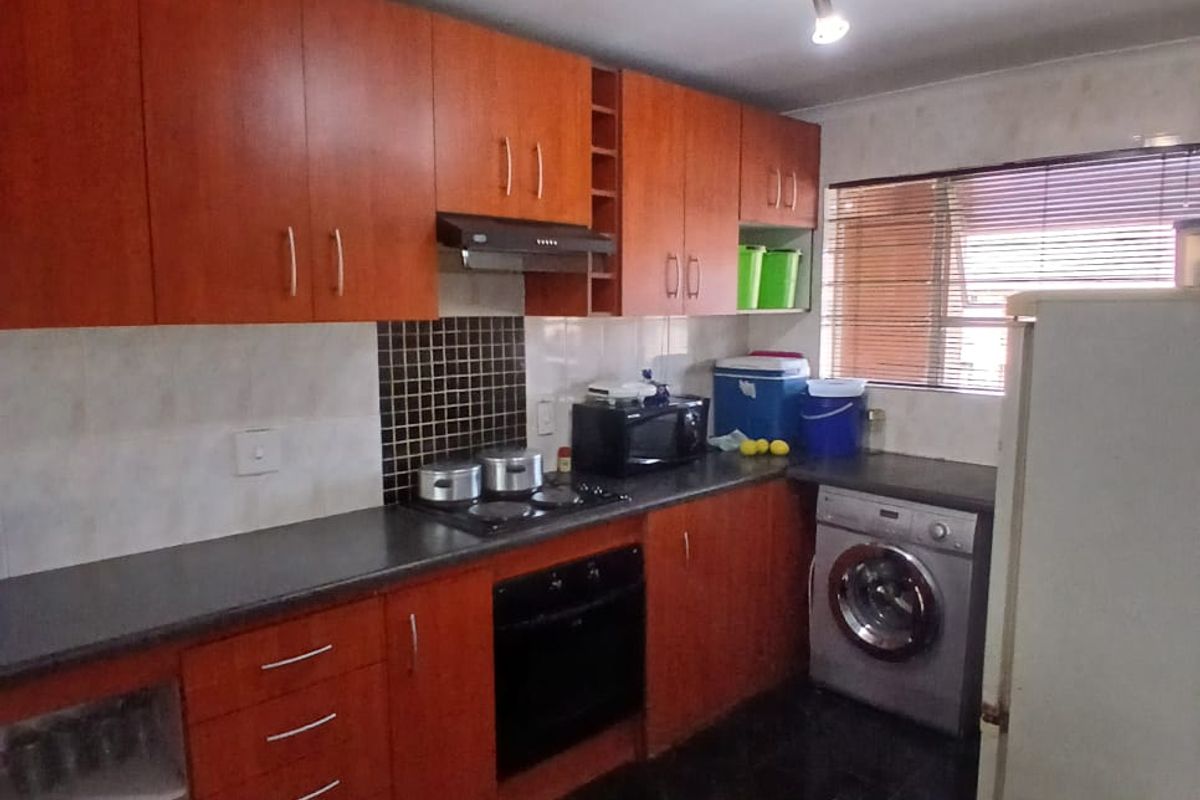 A functional kitchen featuring wood-look cabinetry, dark countertops, built-in oven, hob, extractor fan, and dedicated space for a washing machine.