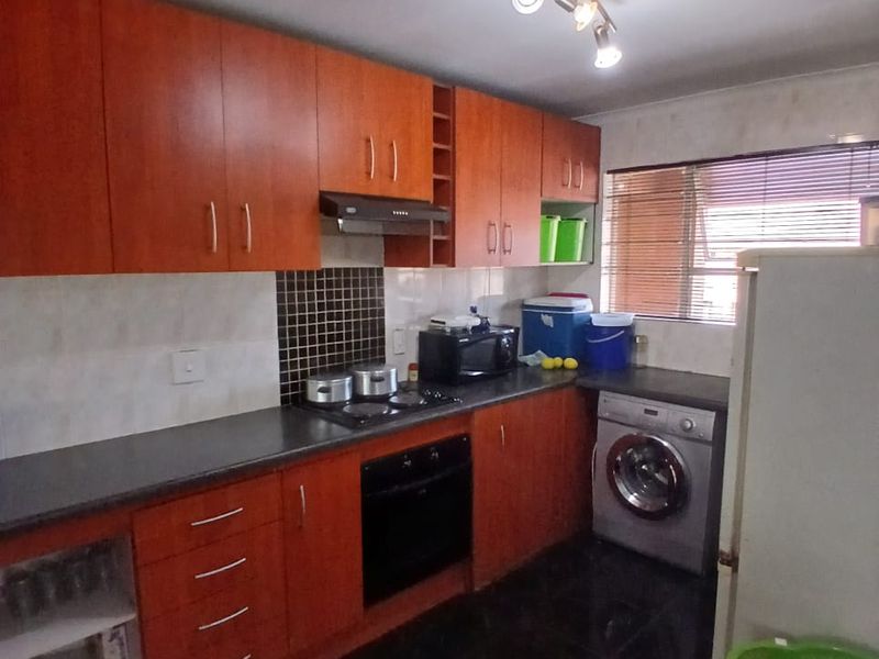 A functional kitchen featuring wood-look cabinetry, dark countertops, built-in oven, hob, extractor fan, and dedicated space for a washing machine.