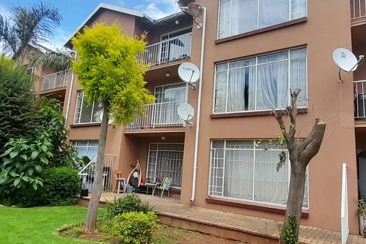 Rear elevation of a multi-story townhouse complex featuring balconies, paved patio areas, and established garden landscaping.