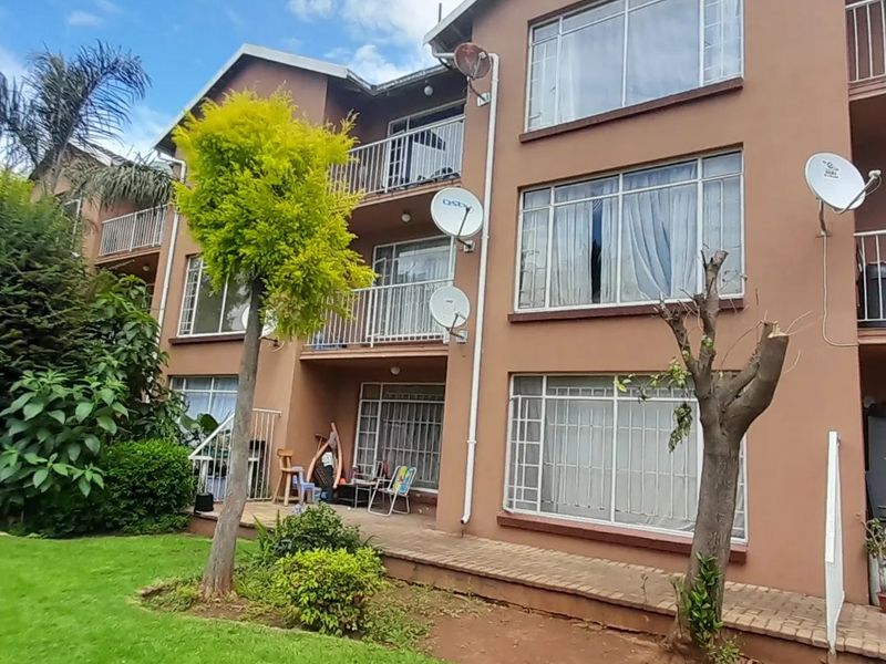 Rear elevation of a multi-story townhouse complex featuring balconies, paved patio areas, and established garden landscaping.