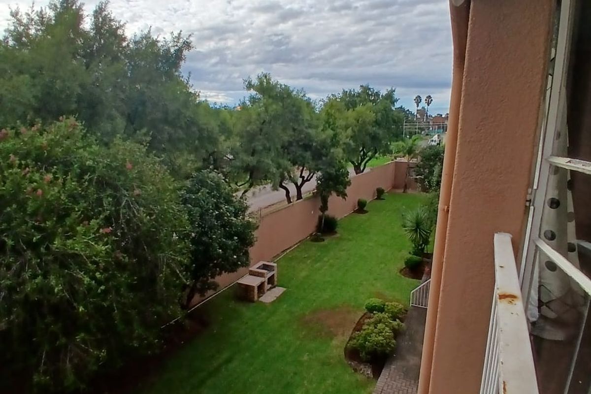 Elevated view of a private rear garden featuring a lawn, paved walkway, and a built-in braai area, viewed from an upper-level balcony.