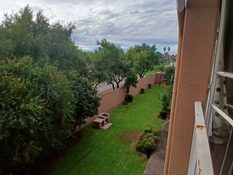 Elevated view of a private rear garden featuring a lawn, paved walkway, and a built-in braai area, viewed from an upper-level balcony.