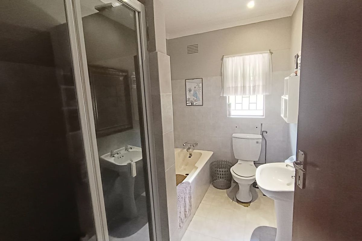 A functional bathroom featuring a shower enclosure, bathtub, pedestal basin, and toilet with neutral tiled finishes.