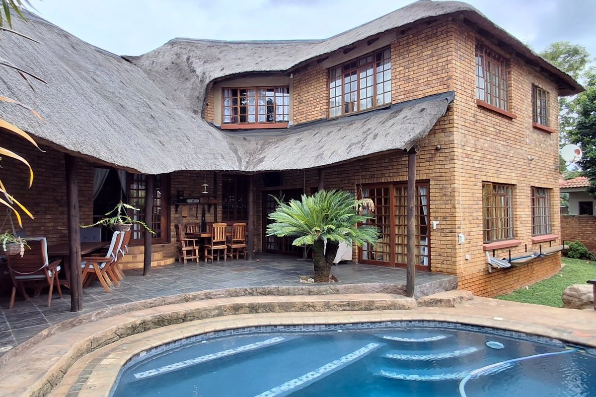 Rear view of a double-story face brick house with a traditional thatched roof, featuring a paved patio area and a swimming pool.