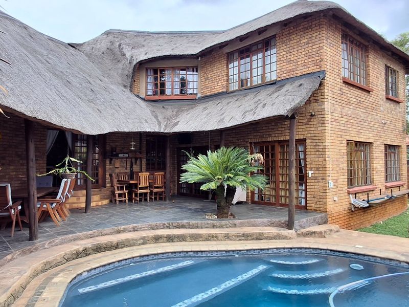 Rear view of a double-story face brick house with a traditional thatched roof, featuring a paved patio area and a swimming pool.