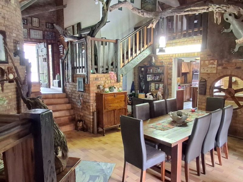 Spacious open-plan living and dining area featuring rustic exposed brick walls, timber staircase, and vaulted ceilings with exposed beams.