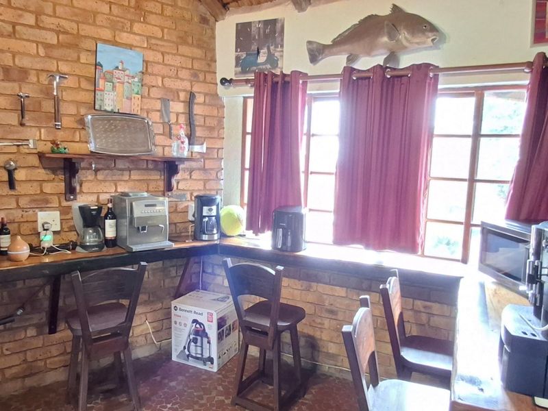 A rustic kitchen area featuring exposed brick walls, built-in timber shelving and wine storage, and a breakfast counter overlooking the window.