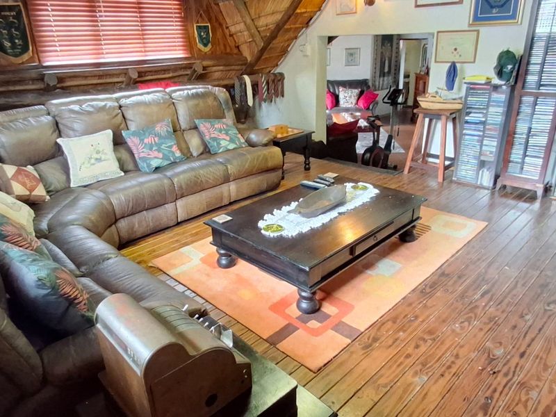 A rustic living room featuring exposed timber roof beams, wood-paneled walls, and polished timber flooring, creating a warm and traditional atmosphere.