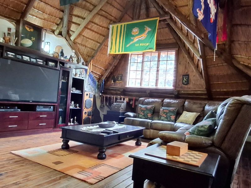 A cozy living room featuring a traditional thatched roof with exposed timber rafters and warm wooden flooring, creating a rustic and inviting atmosphere.