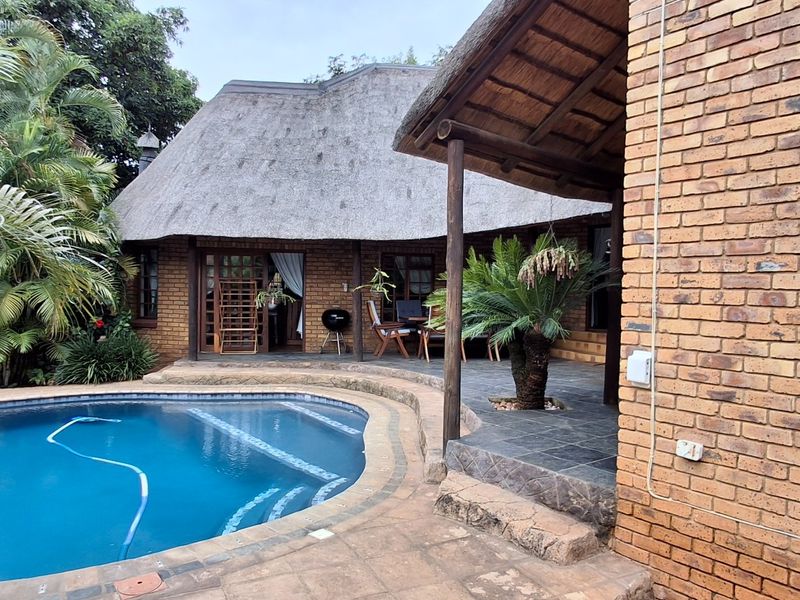 Outdoor pool area featuring a swimming pool, slate patio, and a charming thatched-roof structure with exposed brick walls.