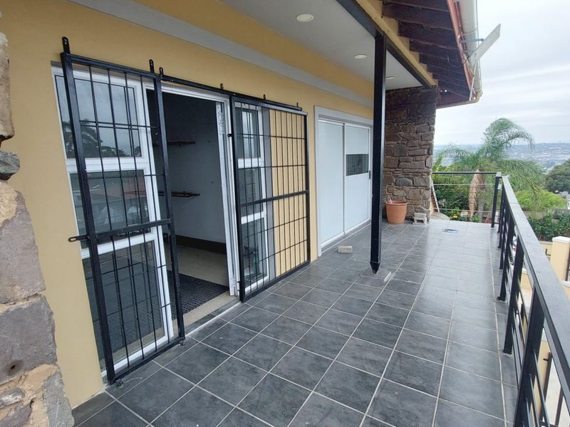 A spacious covered balcony featuring dark tiled flooring, stone cladding accents, and secure sliding door access, offering elevated views of the surrounding area.