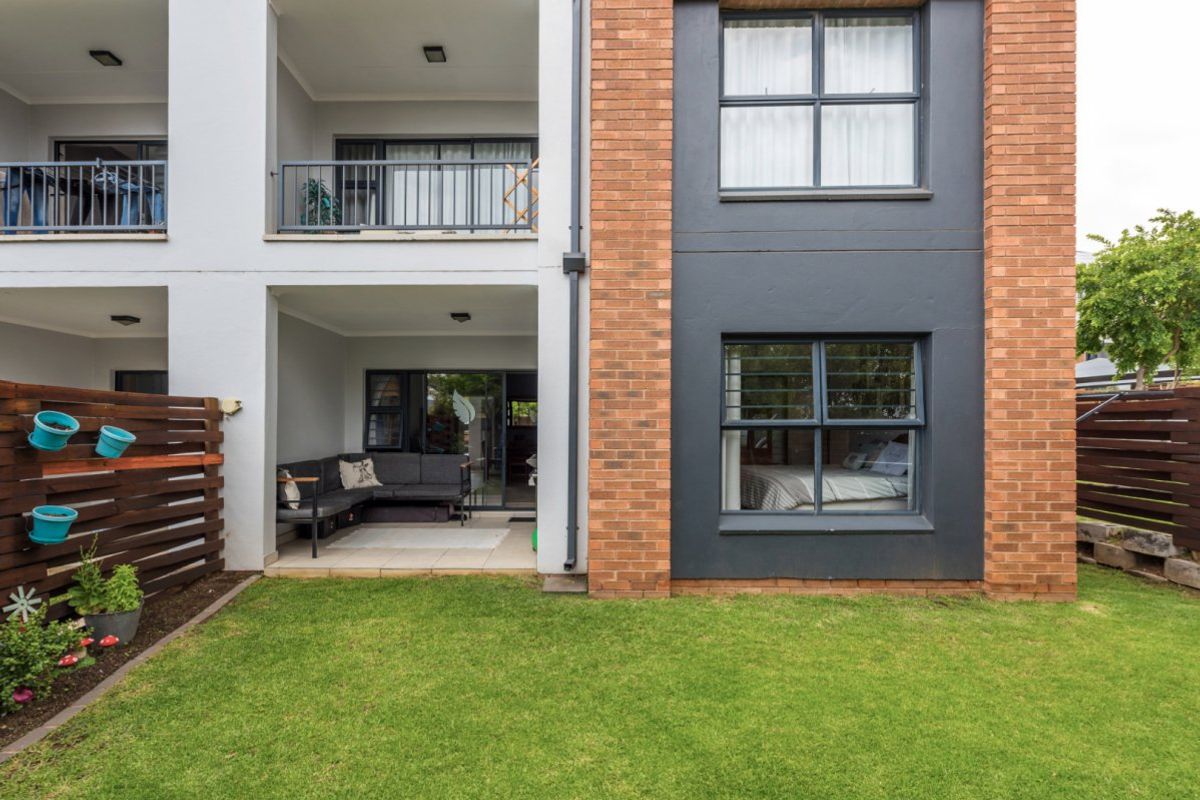 Rear view of the apartment building featuring a ground-floor patio, a private garden area, and a balcony on the upper level.