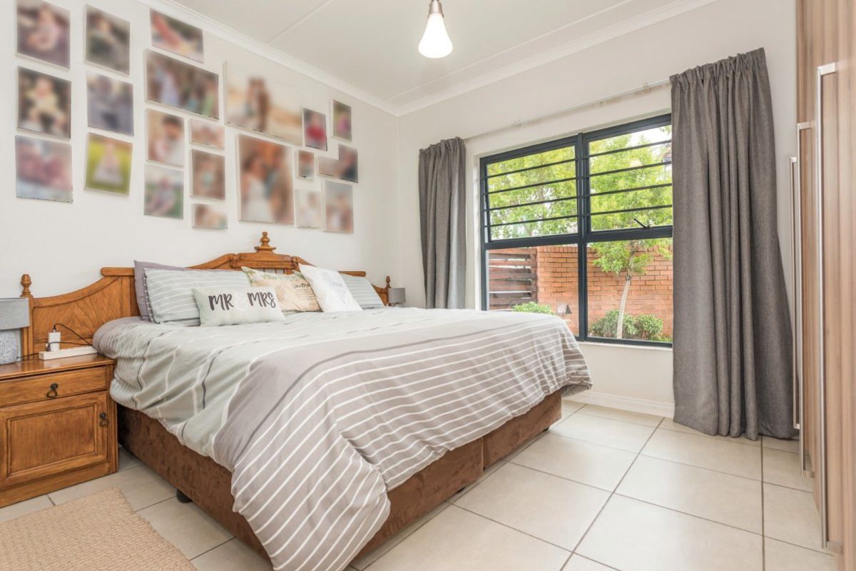 A well-maintained bedroom featuring tiled flooring, built-in cupboards, and a window with security bars overlooking the rear garden area.
