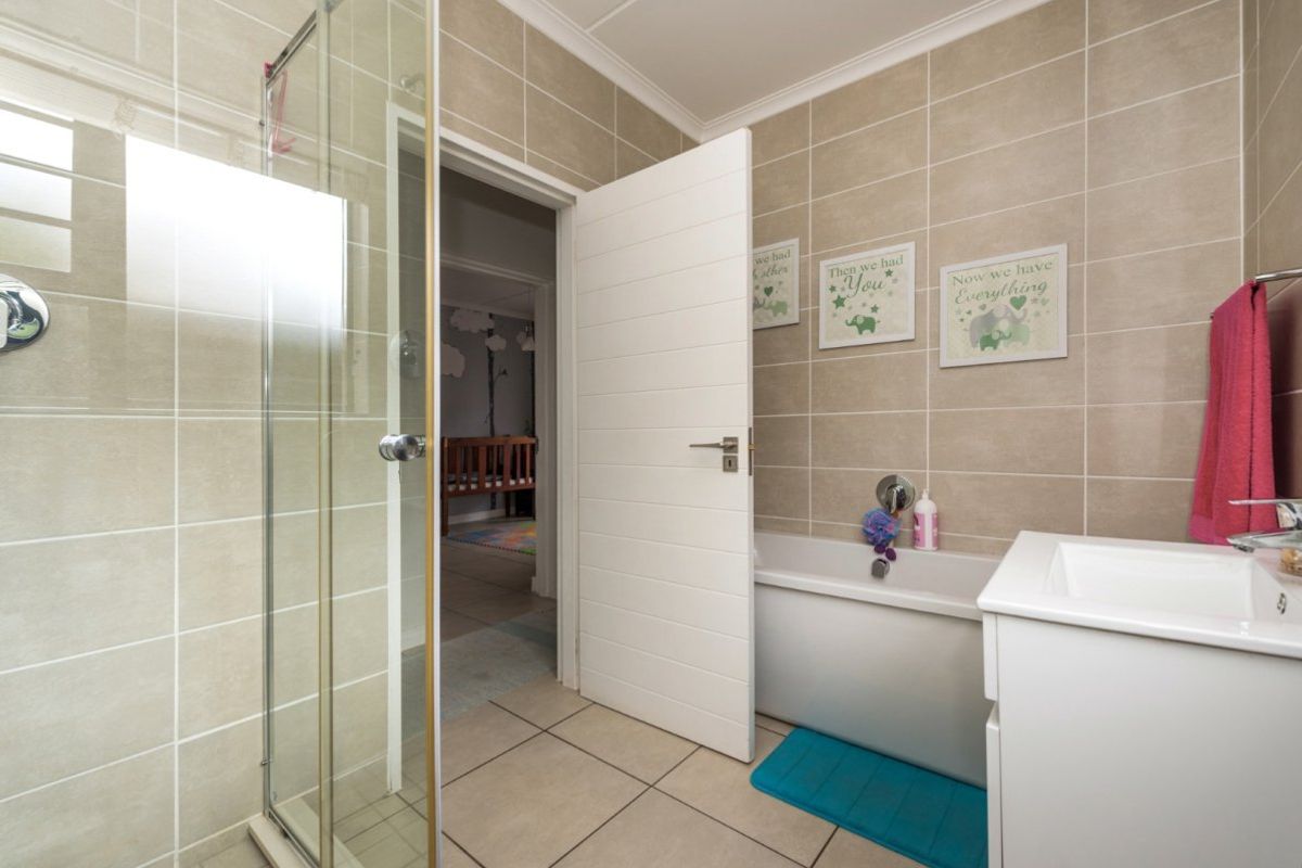 A well-maintained bathroom featuring a glass shower enclosure, a built-in bathtub, and a vanity basin with neutral ceramic tiling throughout.