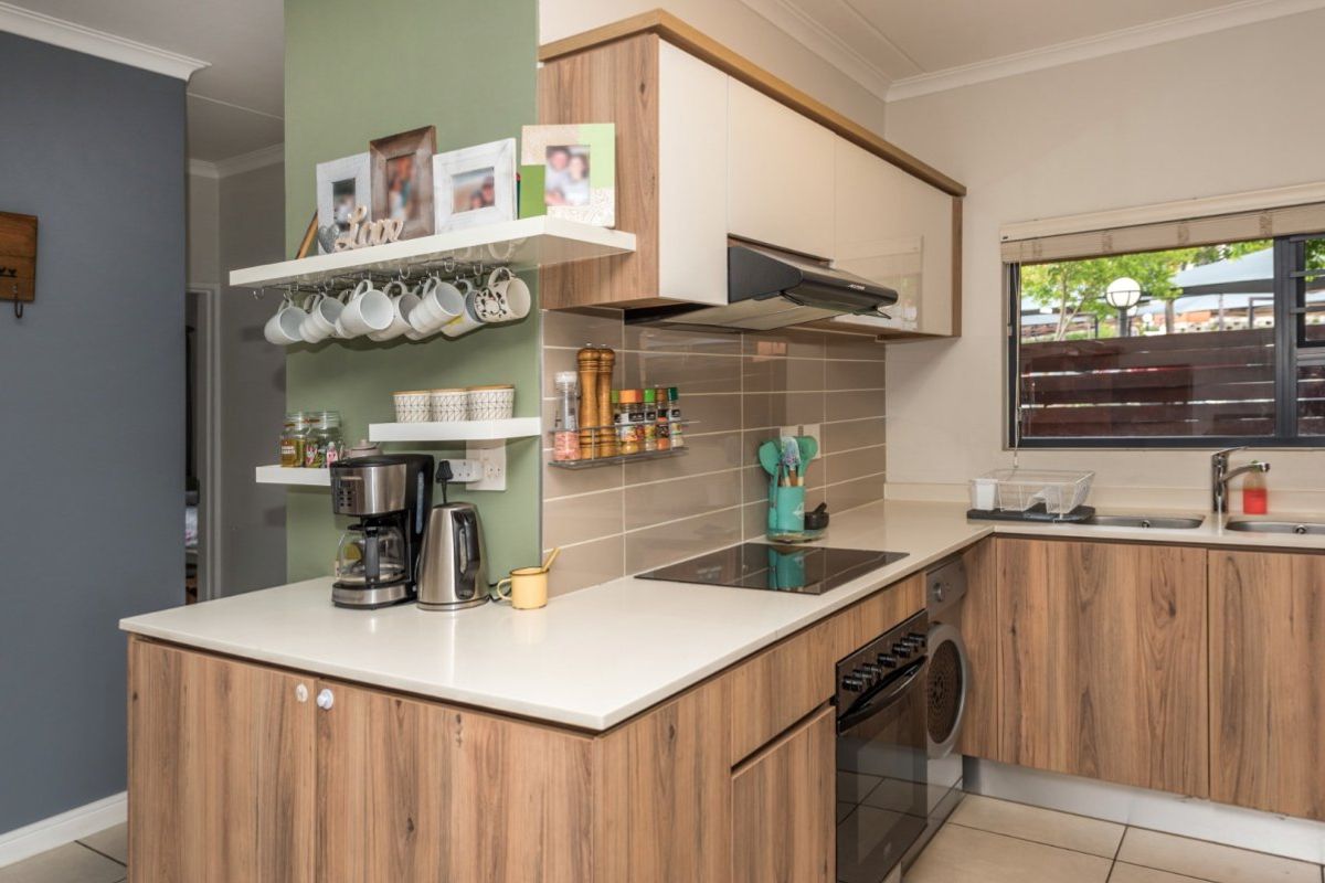 Modern kitchen featuring wood-grain cabinetry, quartz countertops, integrated electric hob, oven, extractor fan, and a tiled backsplash with a functional sink area.