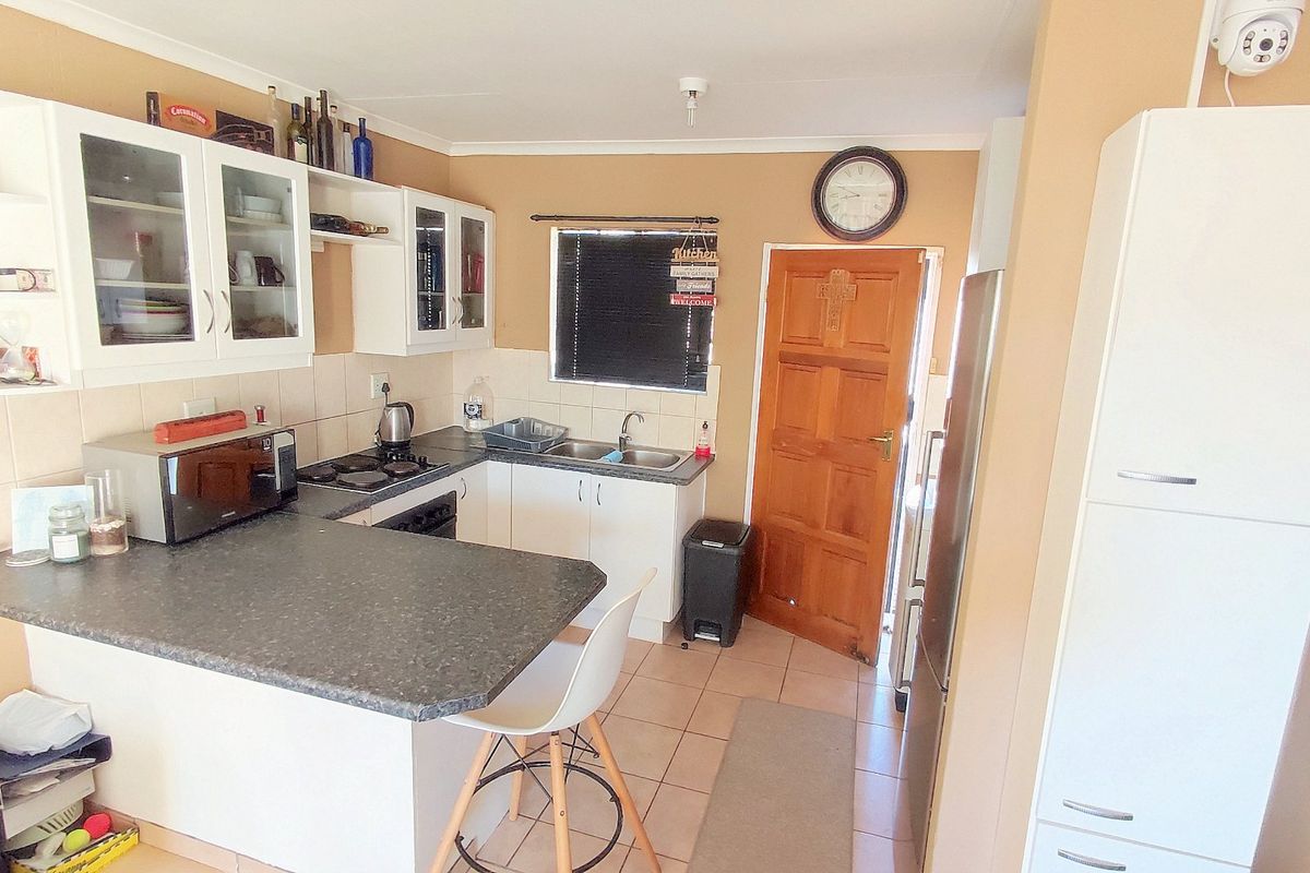 A functional kitchen featuring white cabinetry, dark laminate countertops, a built-in hob and oven, tiled backsplash, and direct access to an exterior door.