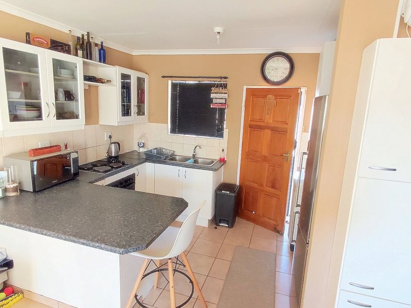 A functional kitchen featuring white cabinetry, dark laminate countertops, a built-in hob and oven, tiled backsplash, and direct access to an exterior door.