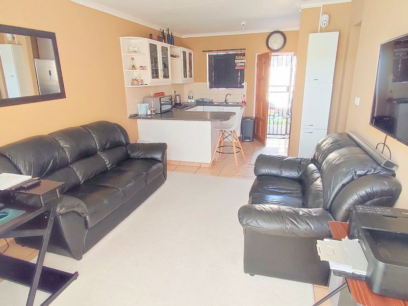 Open-plan living area featuring a compact kitchen with built-in cabinetry, breakfast counter, and tiled flooring, providing a functional layout for daily living.