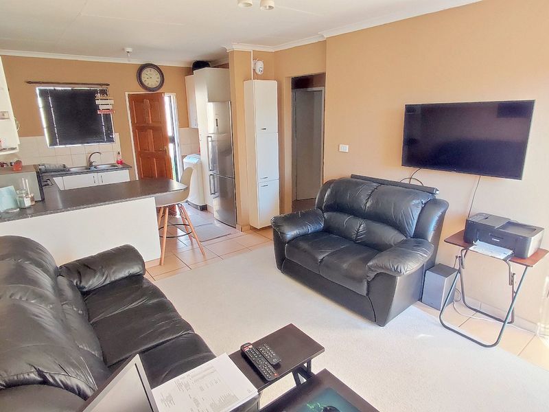 Open-plan living area featuring a functional kitchen with breakfast counter, tiled flooring, and neutral wall finishes, creating a practical and connected living space.