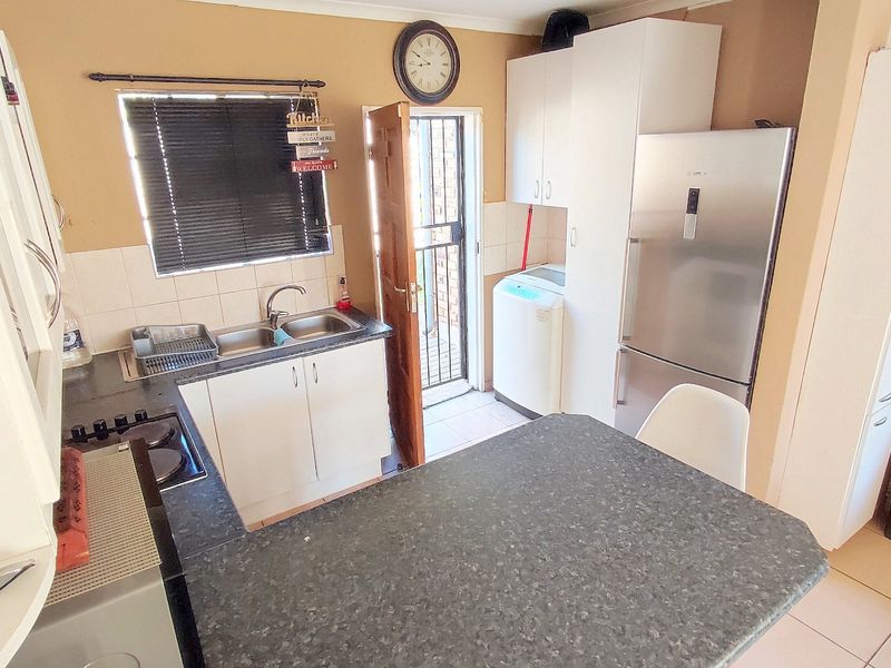 Compact kitchen featuring built-in cabinetry, a double basin sink, hob, and tiled backsplash with direct access to an outdoor area.