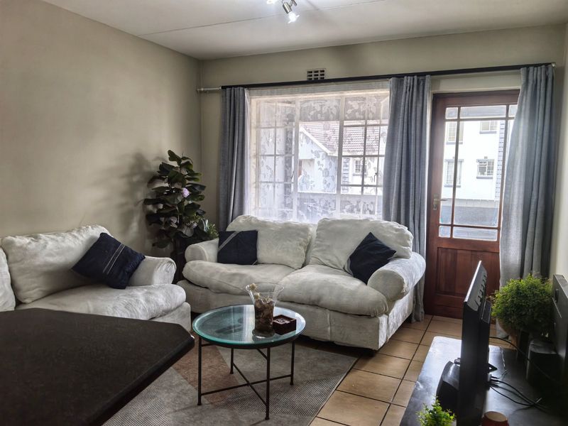 A comfortable living room featuring tiled flooring, a large window for natural light, and a timber-framed glass door leading to the exterior.