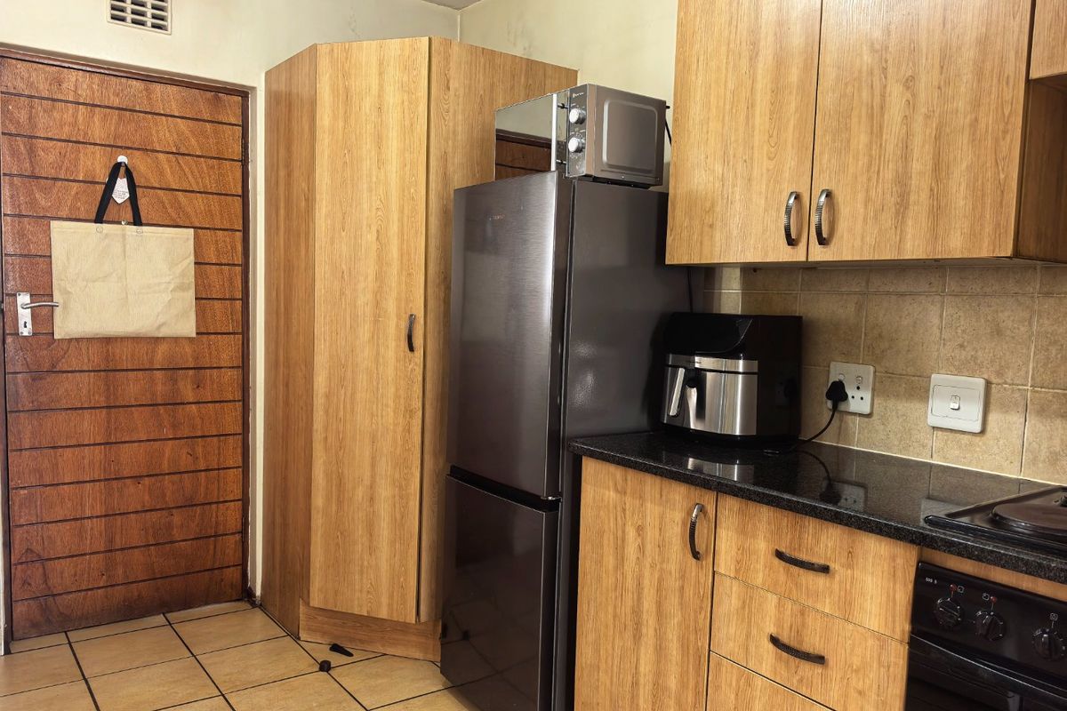 A functional kitchen featuring wood-look laminate cabinetry, granite countertops, and a built-in oven, with tiled flooring and a ventilation grille.