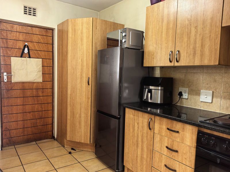 A functional kitchen featuring wood-look laminate cabinetry, granite countertops, and a built-in oven, with tiled flooring and a ventilation grille.