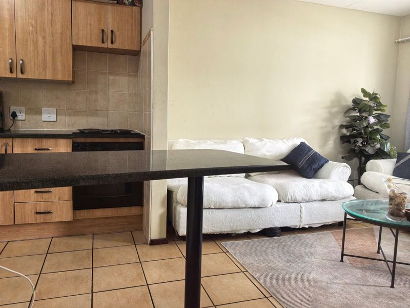 Open-plan living area featuring a compact kitchen with wood-finish cabinetry, granite countertops, and tiled flooring, seamlessly connected to the adjacent living space.