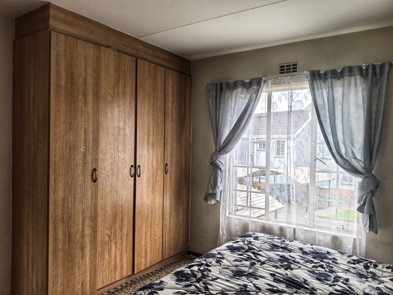 A bedroom featuring a large built-in wooden wardrobe and a window with security bars, offering a view of the surrounding residential area.