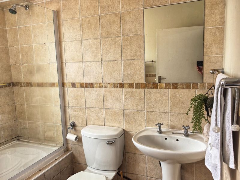 A functional bathroom featuring a pedestal basin, shower enclosure, and neutral ceramic wall tiling with a decorative mosaic border.
