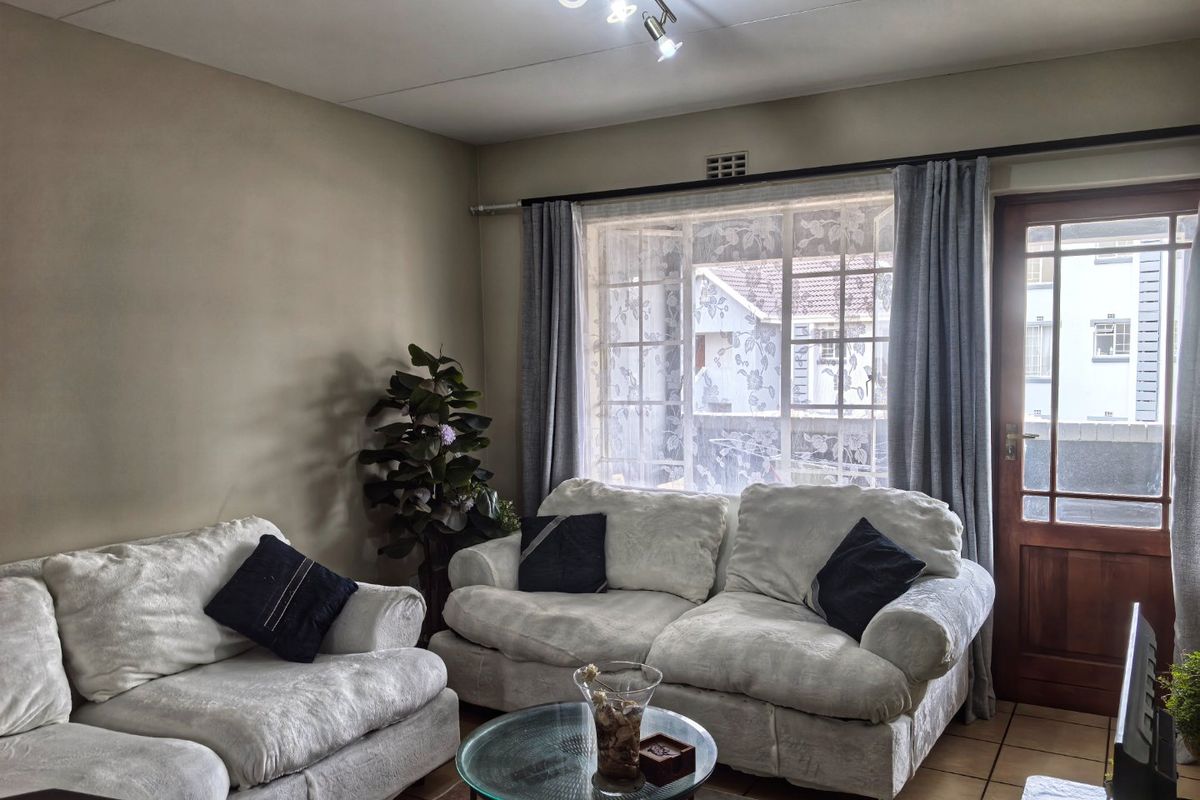 A comfortable living room featuring tiled flooring, a timber-framed exterior door, and a window with security bars, providing natural light and access to the outdoors.