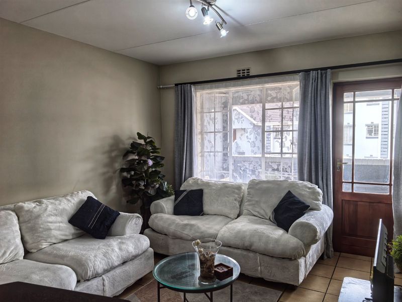 A comfortable living room featuring tiled flooring, a timber-framed exterior door, and a window with security bars, providing natural light and access to the outdoors.