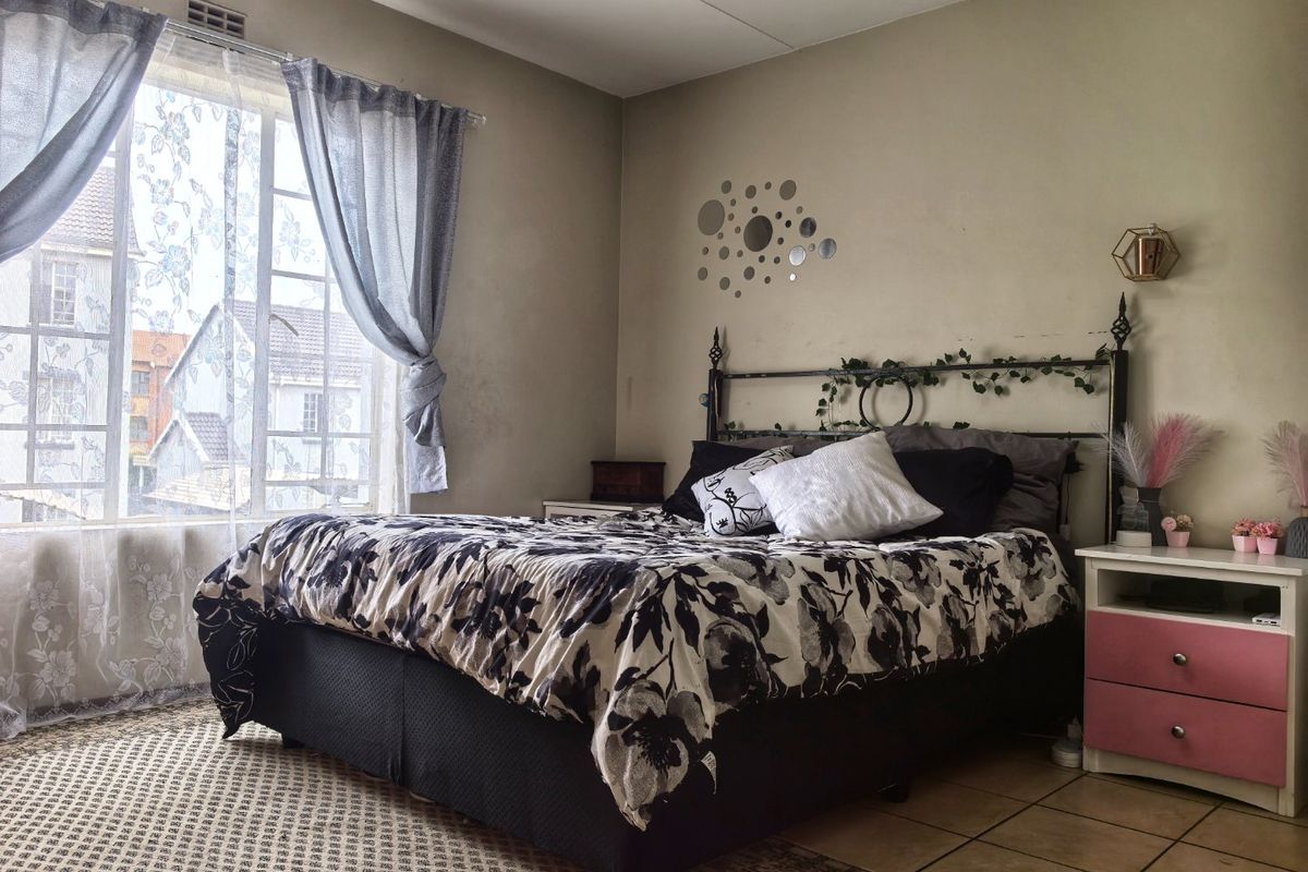 A bedroom featuring tiled flooring and a large window that provides natural light. The walls show signs of wear and could benefit from refreshing.