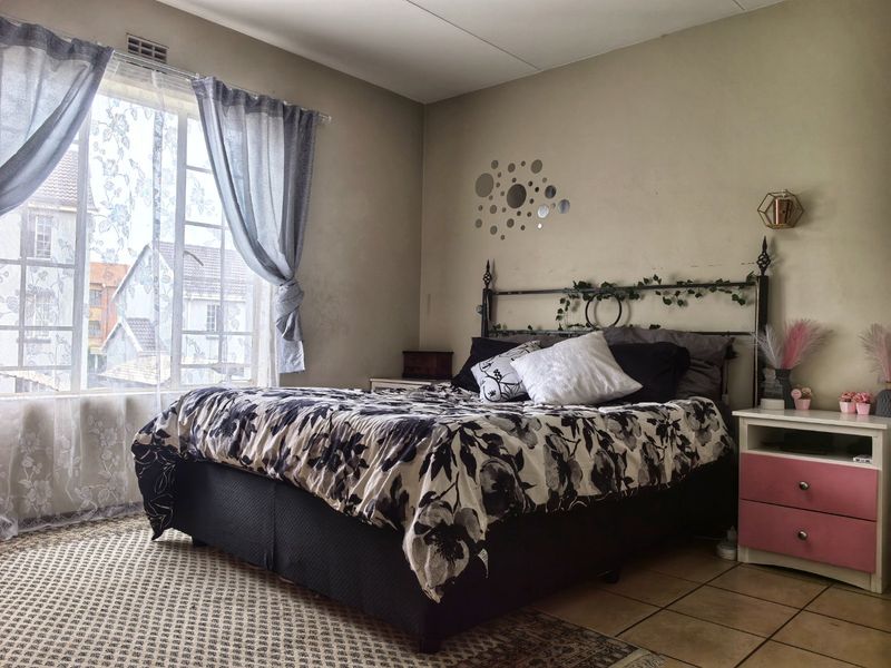 A bedroom featuring tiled flooring and a large window that provides natural light. The walls show signs of wear and could benefit from refreshing.