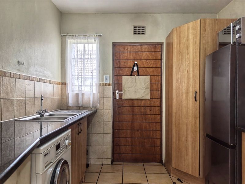 A functional scullery area featuring built-in cabinetry, a stainless steel sink, tiled backsplash, and tiled flooring, providing practical utility space.