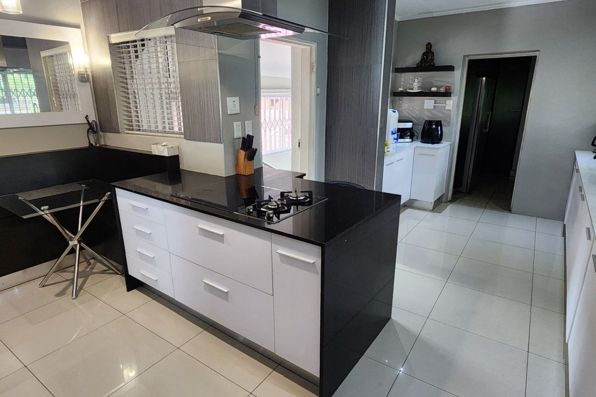 Modern kitchen featuring a central island with gas hob, sleek cabinetry, stone countertops, and tiled flooring, offering a functional and contemporary cooking space.