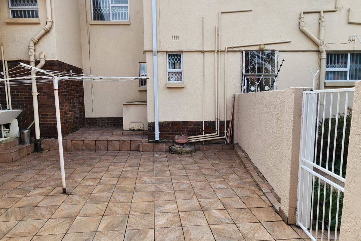 A paved rear courtyard area featuring a utility sink, security gates, and exterior brick and plaster finishes.