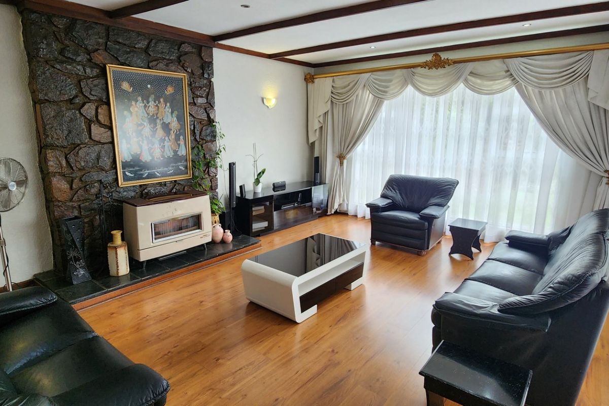 Spacious living room featuring a prominent stone fireplace, warm laminate flooring, and exposed ceiling beams, offering a cozy and traditional atmosphere.
