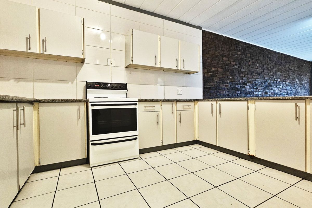A functional kitchen featuring built-in cabinetry, granite countertops, a freestanding stove, and a distinctive exposed brick feature wall.