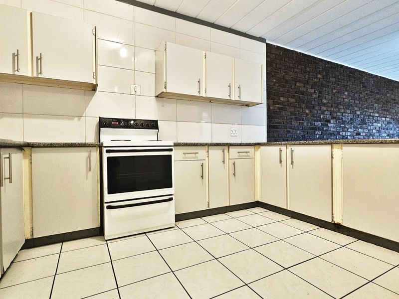 A functional kitchen featuring built-in cabinetry, granite countertops, a freestanding stove, and a distinctive exposed brick feature wall.