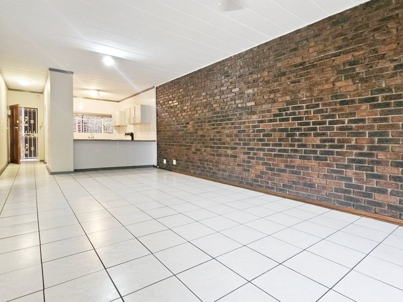 Spacious open-plan living area featuring a prominent exposed brick wall, neutral ceramic floor tiles, and an adjoining kitchen space.