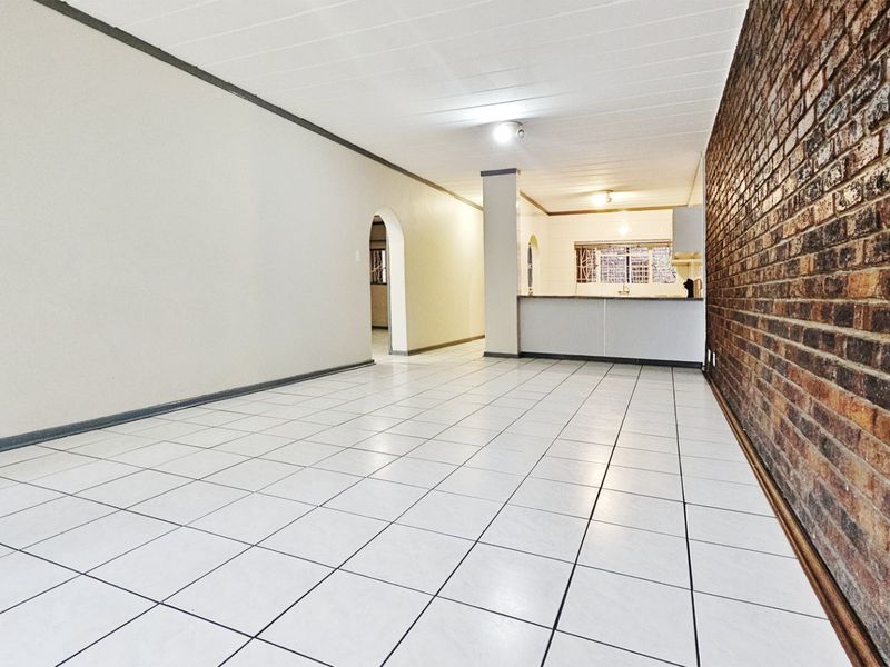 Spacious open-plan living and kitchen area featuring a distinctive exposed brick wall, neutral tiled flooring, and a functional breakfast counter.