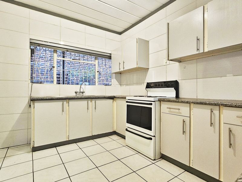 A functional kitchen featuring tiled walls and flooring, granite countertops, built-in cabinetry, and a freestanding stove with a window overlooking the exterior.