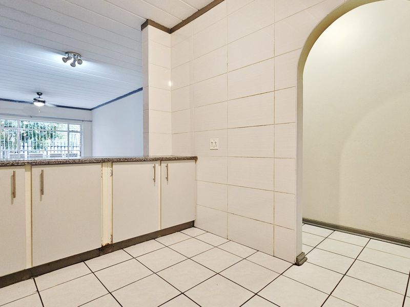 A functional kitchen area featuring tiled walls and flooring, granite countertops, and built-in cabinetry, leading through an archway to the adjacent living space.