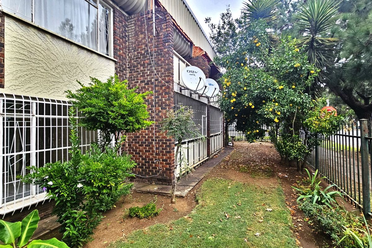 Rear exterior view of the apartment building featuring face brick facade, security bars on windows, and a small garden area with perimeter fencing.