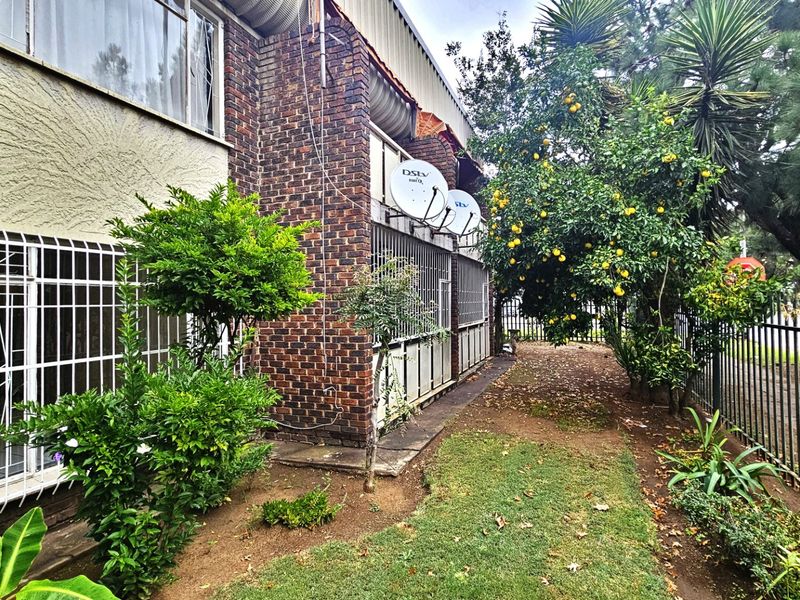 Rear exterior view of the apartment building featuring face brick facade, security bars on windows, and a small garden area with perimeter fencing.