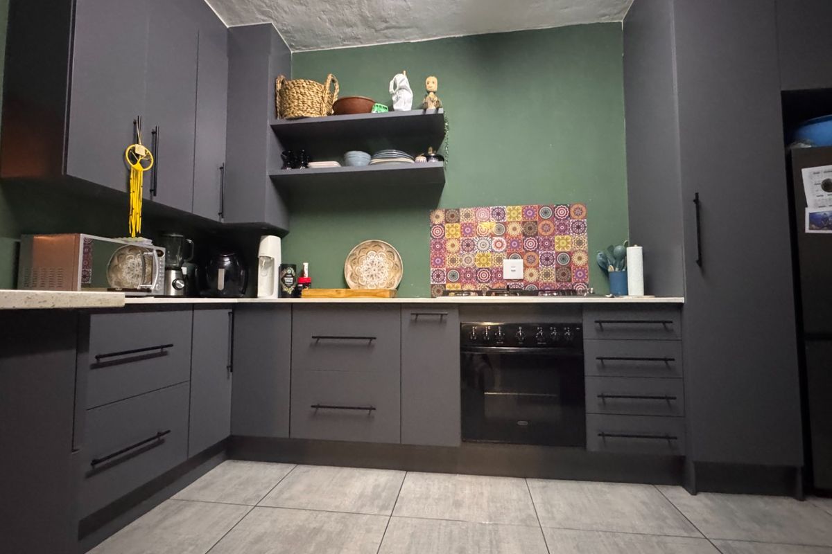 Modern kitchen featuring dark grey cabinetry, stone countertops, built-in oven, gas hob, and decorative tiled splashback with large format floor tiles.