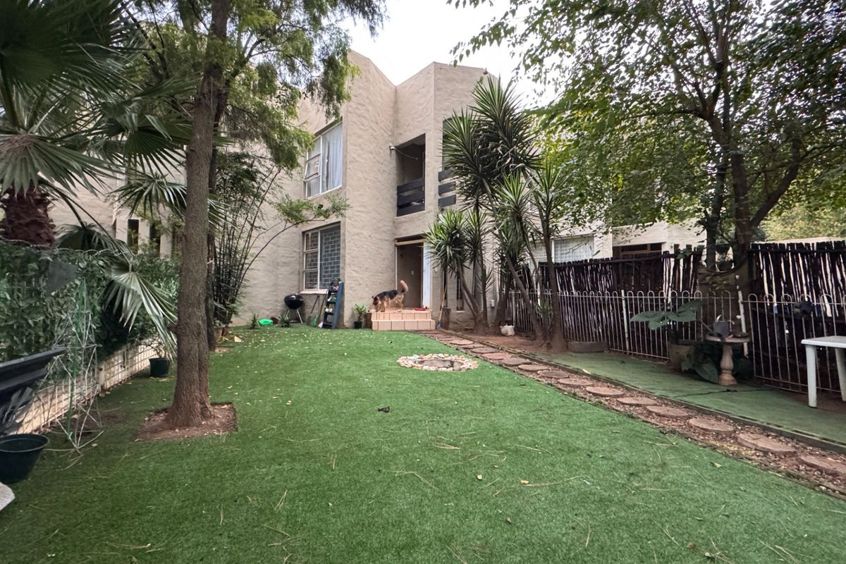 Rear view of the townhouse featuring a private garden with artificial lawn, stone pathway, and a small raised patio area.