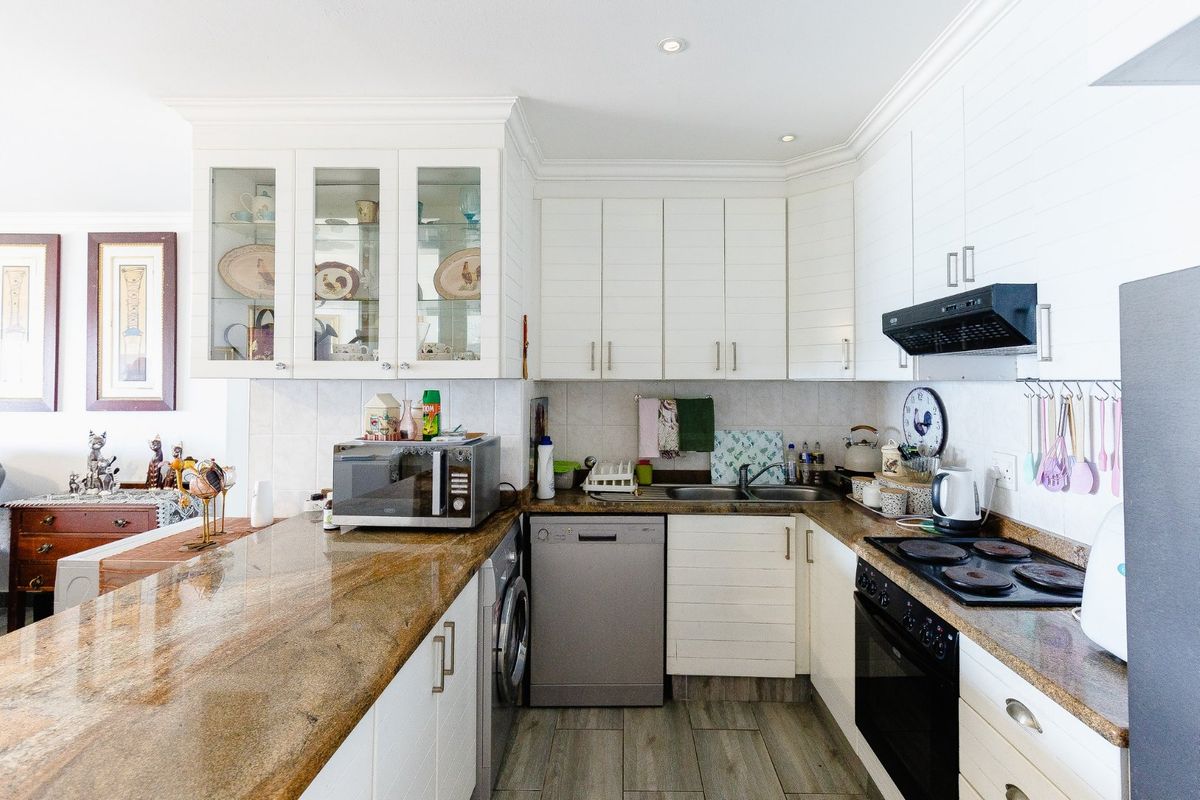 A well-maintained kitchen featuring granite countertops, white cabinetry, glass-fronted display units, and integrated appliances including an oven and hob.